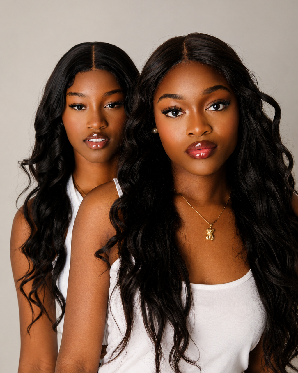 Two women with long, wavy hair sitting side by side against a neutral background
